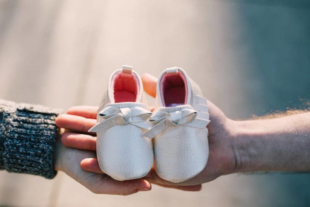two hands holding a pair of baby shoes